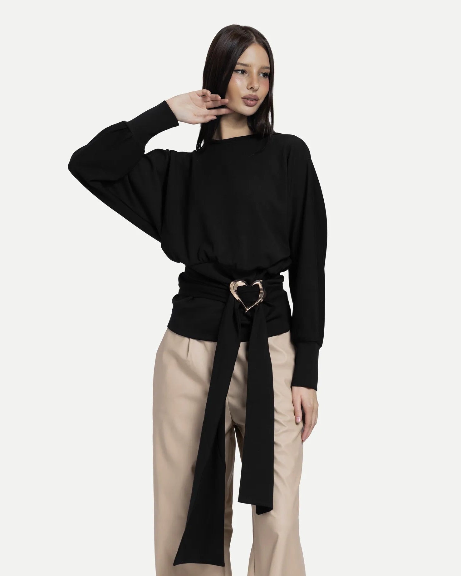 Woman wearing a black top and beige pants with a belt on a white background